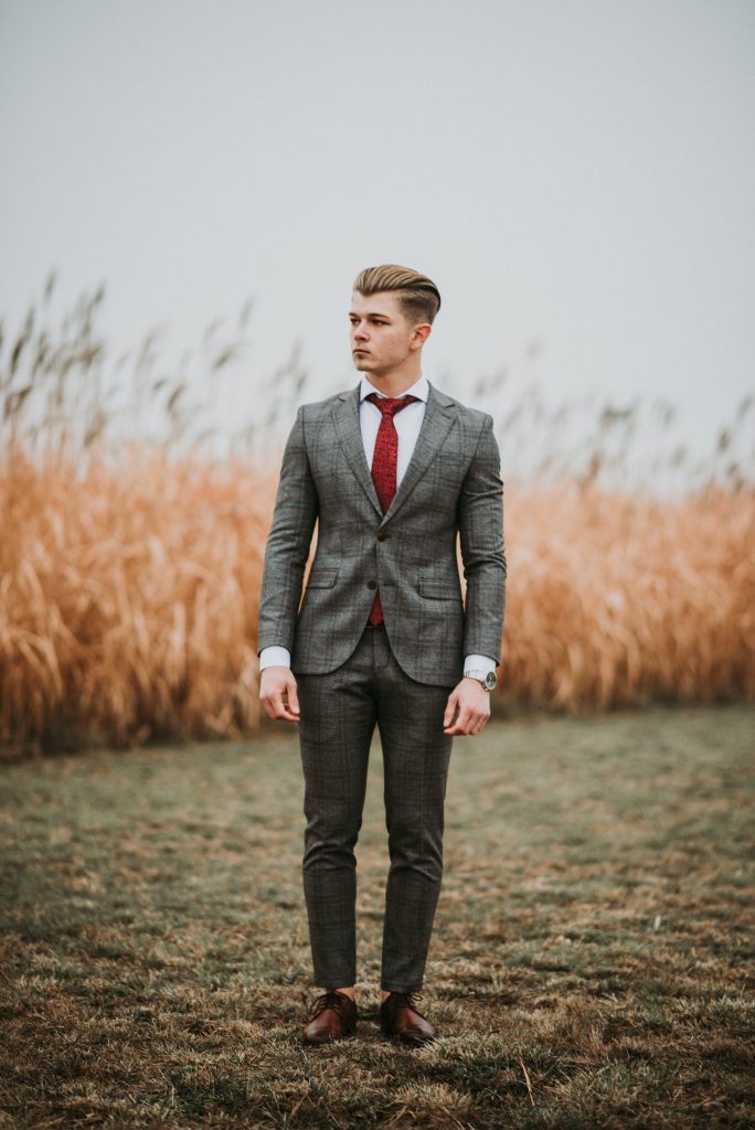 Jeune homme habillé en costume gris, chemise blanche et cravate rouge