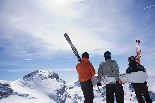 Trois personnes de dos, en tenue de ski, au sommet d'une montagne