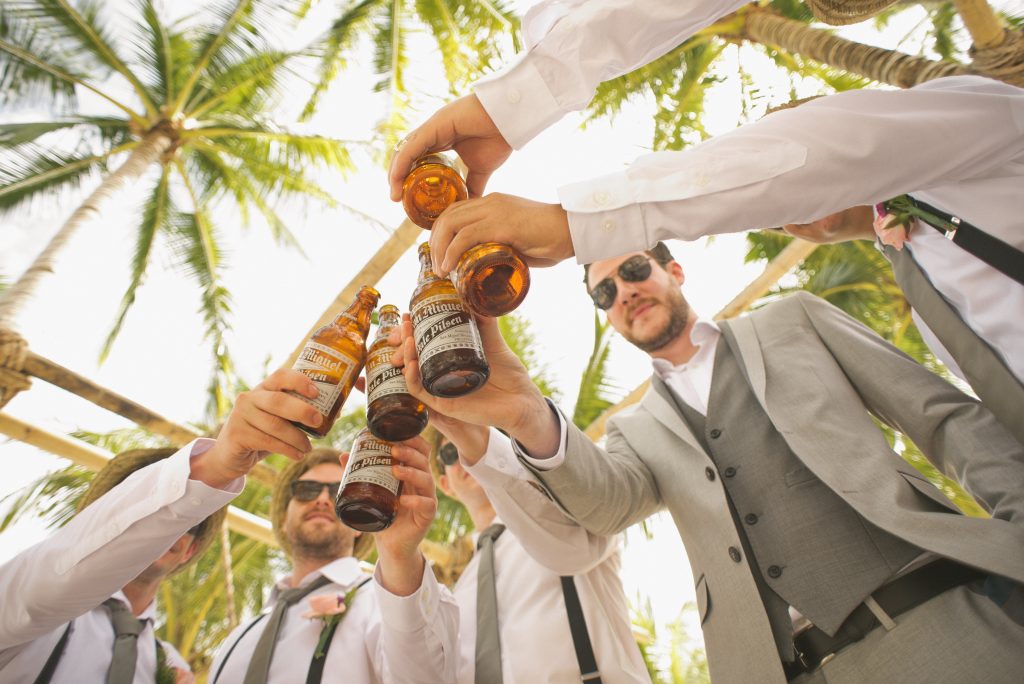 Groupe d'hommes en costumes et lunettes de soleil qui trinquent avec des bouteilles de bière