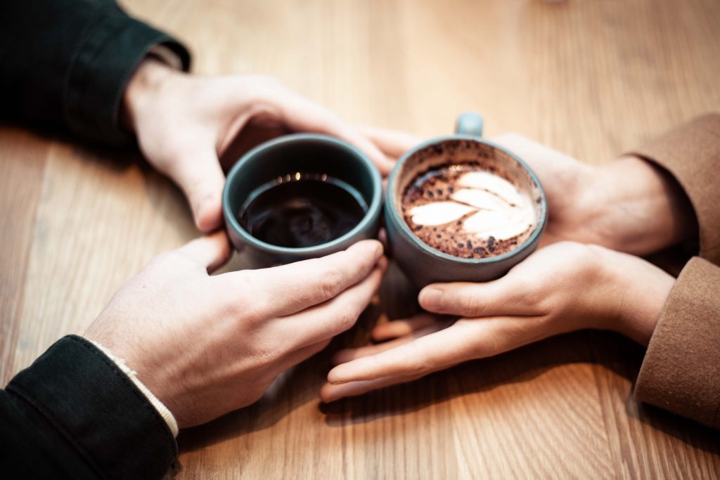 Gros plan sur les mains d'un homme et d'une femme, regroupées au milieu de la table avec des chocolats chauds