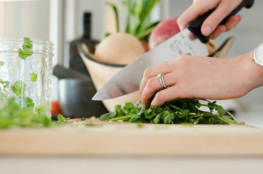 zoom sur les mains d'une femme qui coupe des herbes aromatiques avec un couteau de cuisine